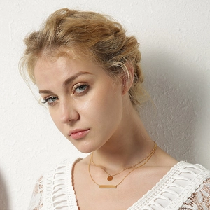 Close-up of gold double layer necklace featuring round disc and horizontal bar pendants