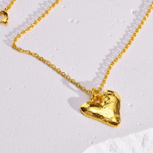 Golden geometric heart necklace with a hammered lava texture on a white stone background