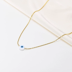 Detail of gold evil eye necklace with blue enamel bead on white silk background