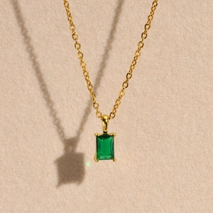 Macro view of a gold-tone necklace featuring a rectangular emerald green zircon pendant
