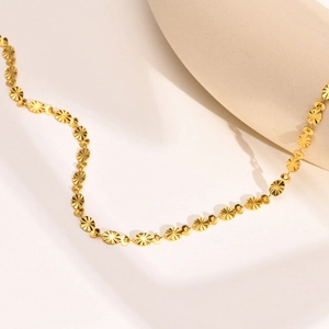 Detail of golden stainless steel necklace with embossed sunburst pattern discs