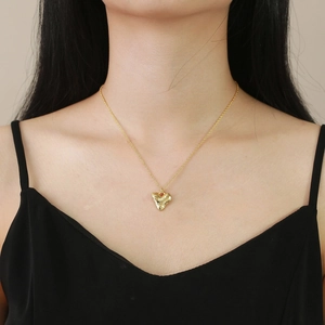 Golden heart necklace with hammered lava texture worn by a model on collarbone
