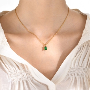 Close-up of a gold necklace featuring a rectangular emerald green zircon pendant on a model