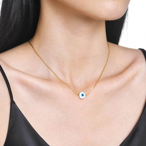 Detail of gold evil eye pendant necklace worn on neck with white disc and blue pupil charm