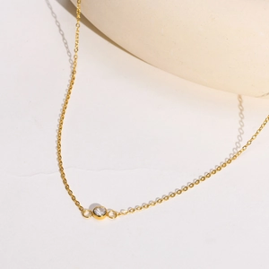 Détail d'un collier fin en acier inoxydable doré avec un pendentif en zircon clair