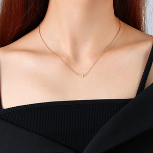 Détail d'un collier avec pendentif M en acier inoxydable doré sur le cou d'une femme