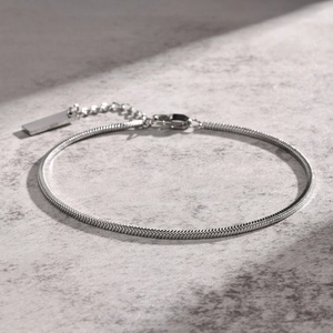 Macro detail of silver snake chain bracelet showing lobster clasp and polished metal tag