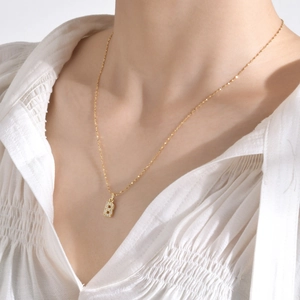 Gros plan d'un collier doré avec pendentif lettre B serti de zircons sur chemise blanche
