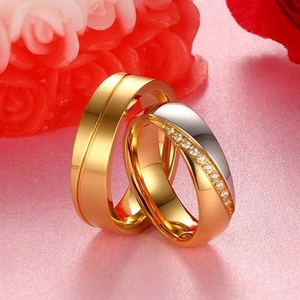 Golden and silver stainless steel couple rings with crystals on a pink floral background