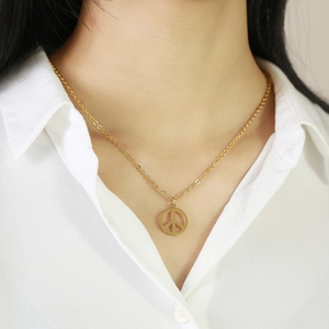 Dettaglio della collana con ciondolo peace dorato su donna in camicia bianca