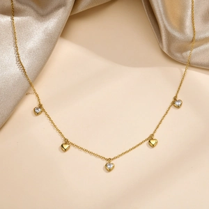 Detail view of gold heart necklace with zircon charms on soft satin background