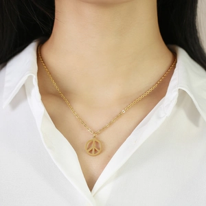 Primo piano di una collana con ciondolo segno della pace dorata su una camicia bianca