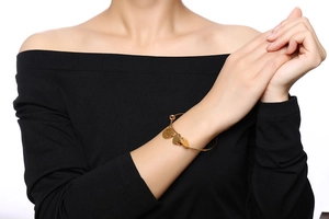 Détail d'un bracelet doré en acier titane avec breloques cœur et feuille sur un poignet