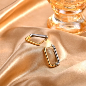 Close-up of two-tone rectangular metal hoop earrings on elegant gold satin fabric