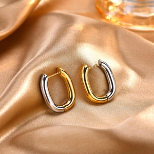 Detail of two-tone gold and silver oval huggie earrings on premium gold silk fabric