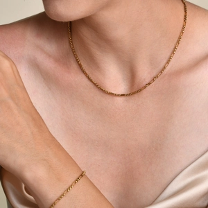 Détail d'un ensemble collier et bracelet dorés portés par un mannequin en soie