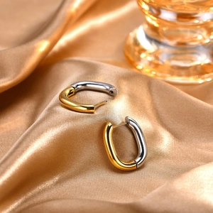 Detail of two-tone oval hoop earrings on elegant gold silk fabric with glass decor