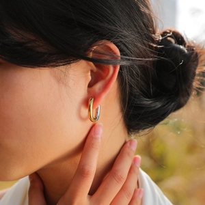 Macro close-up of a bi-color gold and silver oval hoop earring on a female model's ear