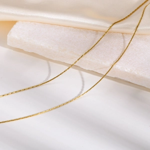 Close-up of a double-layered golden chain necklace on silk fabric with elegant lighting