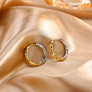 Close-up of two-tone hoop earrings with geometric triangular cut texture on gold satin