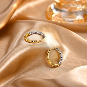 Detail of two-tone stainless steel geometric earrings on elegant gold silk fabric
