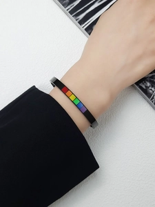 Detail of black stainless steel C-shape open bracelet with rainbow striped inlay on wrist