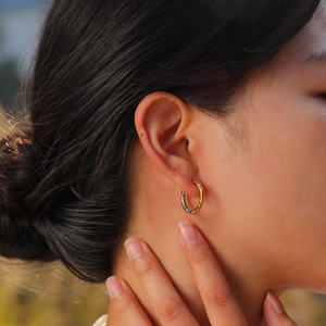 Detail of two-tone stainless steel hoop earrings with diamond pattern on a female model