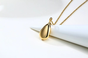 Macro detail of a polished gold teardrop urn pendant on a minimalist white display