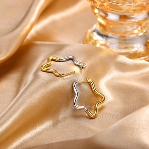 Close-up of two-tone wave star earrings in gold and silver finish on silk fabric