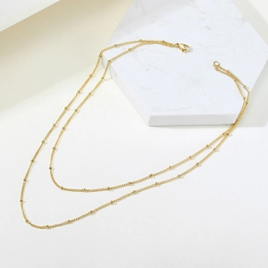 Detail of double-layer gold bead chain necklace with lobster clasp in a minimalist style