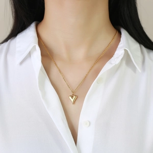 Gros plan du collier avec pendentif cœur doré poli porté sur une chemise blanche
