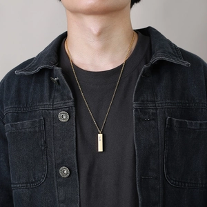 Men's gold vertical bar urn necklace with zircon inlay worn over a denim jacket