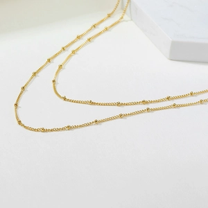 Detail view of a 2mm gold satellite chain necklace with delicate beads on a marble surface