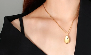 Close-up of a gold teardrop urn pendant worn on a model against a black suit background
