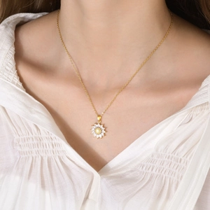 Detalle de un collar con colgante de girasol dorado y gemas de marquesa blancas