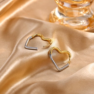 Close-up of two-tone heart earrings in gold and silver finish on luxury silk