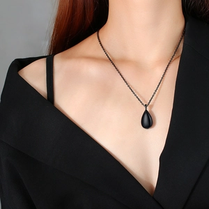Macro detail of teardrop-shaped matte black urn pendant on a matching fine ring chain