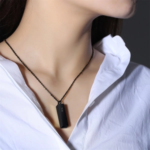 Detail shot of a matte black cylinder pendant necklace worn with a casual white shirt