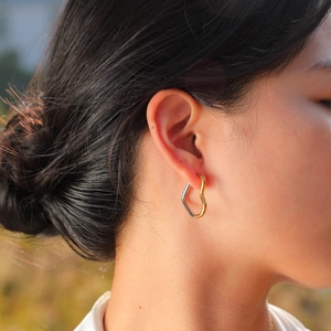 Close-up of model wearing two-tone heart-shaped geometric hoop earrings in a natural setting