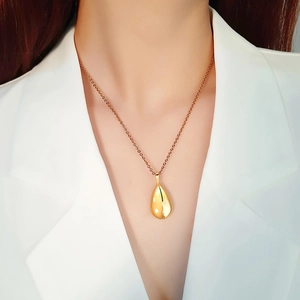 Close-up of polished gold teardrop pendant necklace worn over a white suit jacket