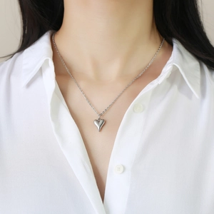 Gros plan d'un collier pendentif cœur minimaliste porté sur une chemise blanche chic