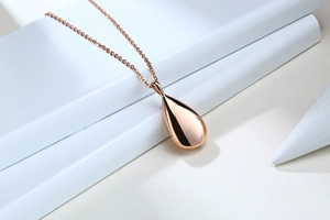 Macro view of rose gold teardrop urn pendant on white geometric display stand