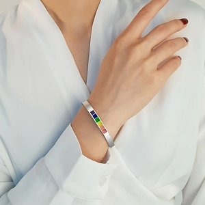 Detail of silver C-shaped cuff bracelet with rainbow enamel squares on model wrist