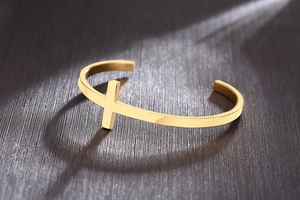Detailed view of a golden polished stainless steel cross cuff bracelet on a textured background