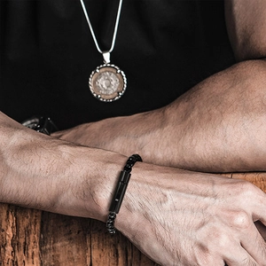 Detail of men's black beaded bracelet with cylinder clasp on vintage wood background