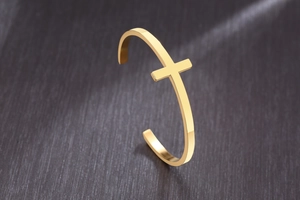 Close-up of a gold stainless steel cross cuff bracelet on a dark metallic background