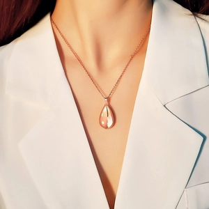 Detailed view of rose gold teardrop pendant necklace worn by a model in a white suit