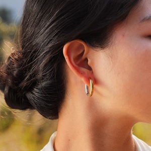 Modern two-tone oval hoop earrings in polished gold and silver on a female model