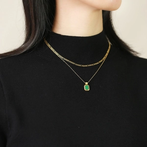 Close-up of gold layered necklace with rectangular green stone pendant on a black sweater