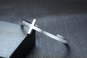 Macro detail of polished stainless steel cross cuff bracelet on a premium gift box